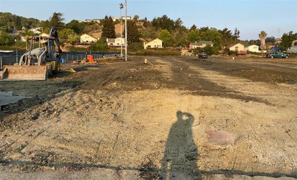 Image of bare field, a human's shadow is visible in the foreground.